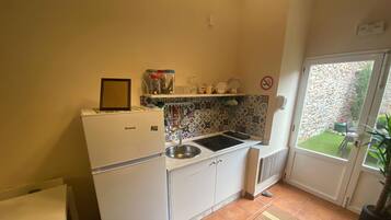 A compact kitchen with white cabinets, a built-in sink, a small refrigerator, and a tiled backsplash.