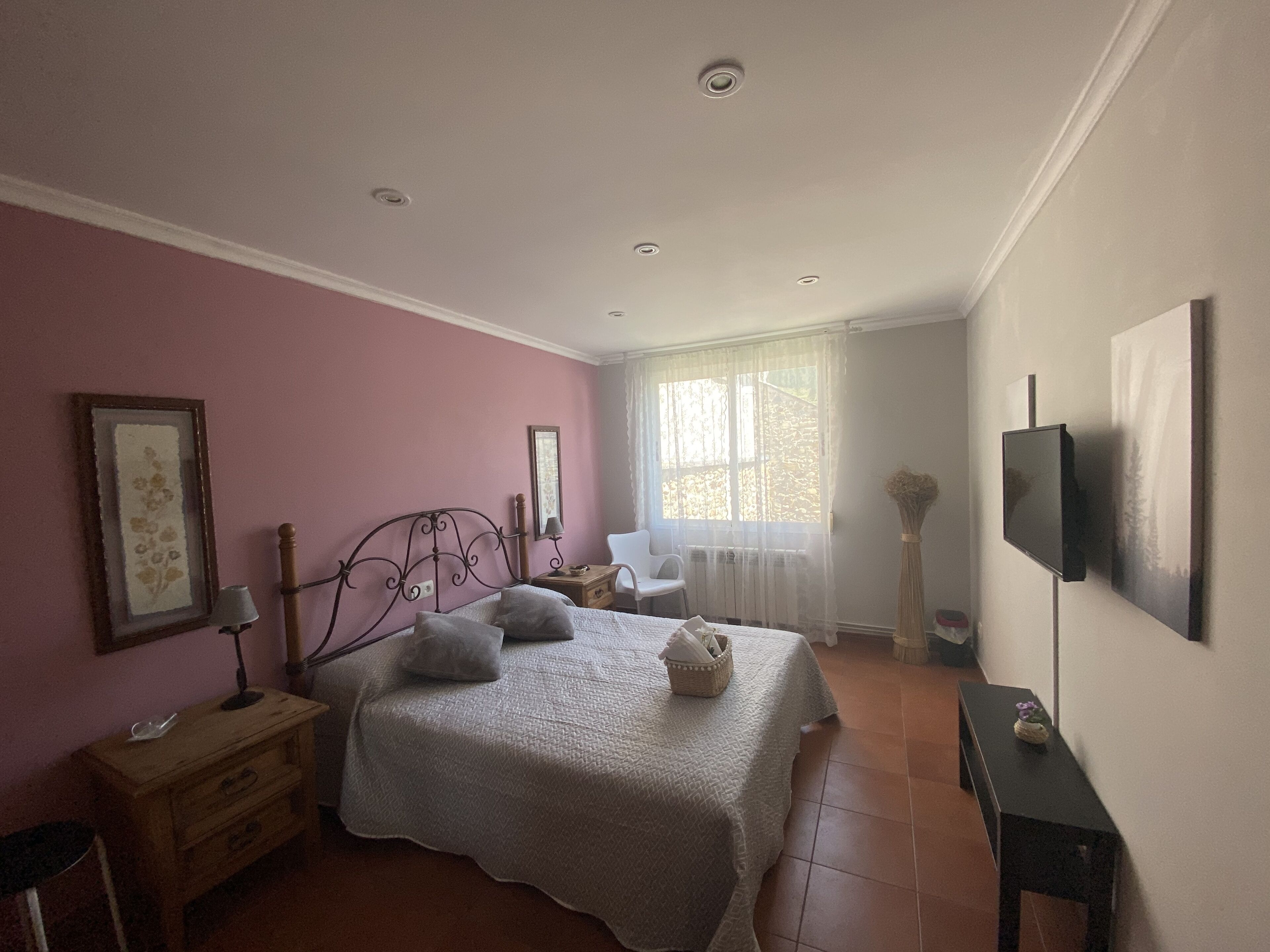 Un dormitorio con cama, mesita de noche, lámpara y televisor en la pared.