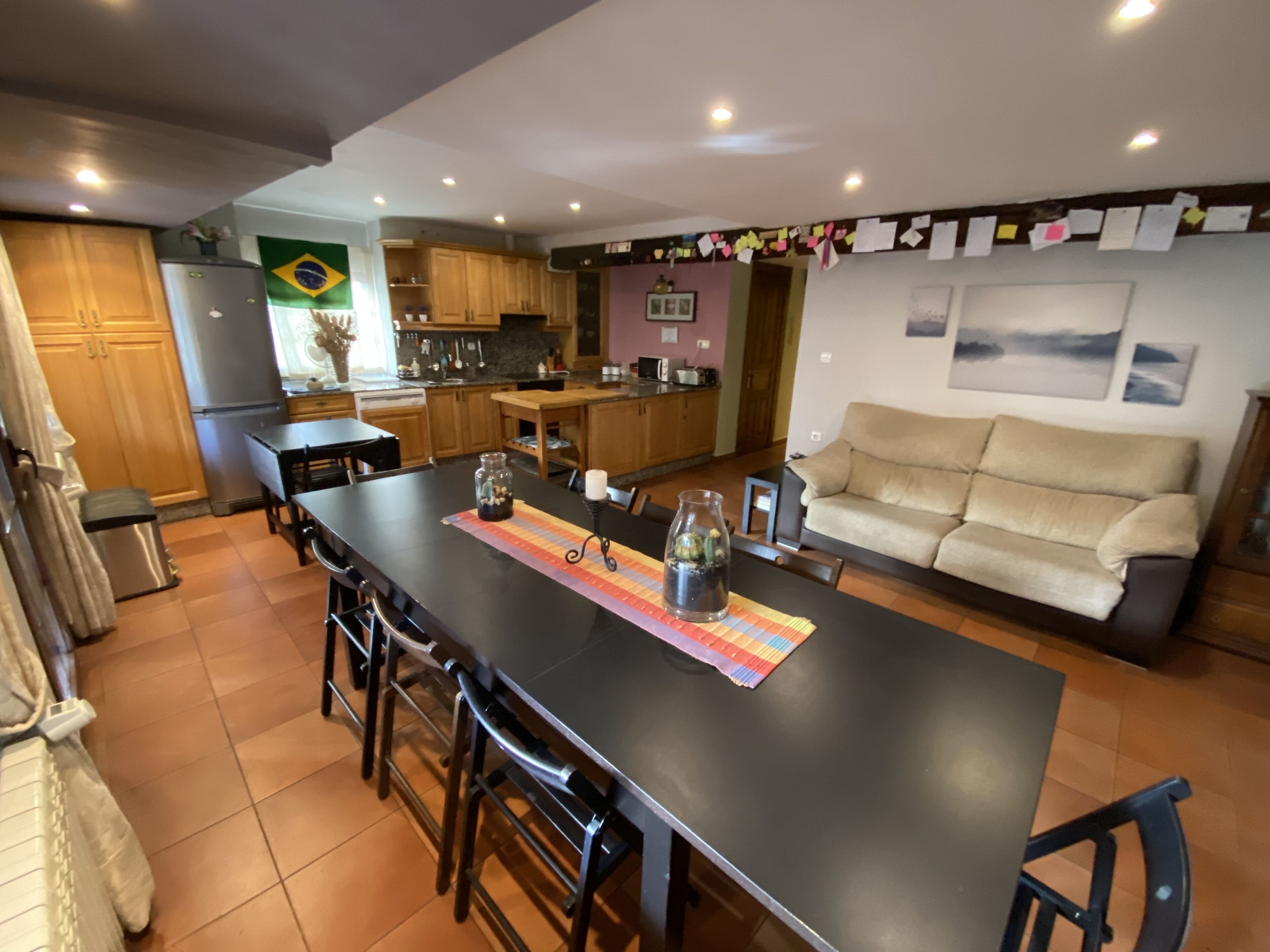 A spacious living area with a large central island, wooden cabinets, a sofa, and a kitchen in the background.