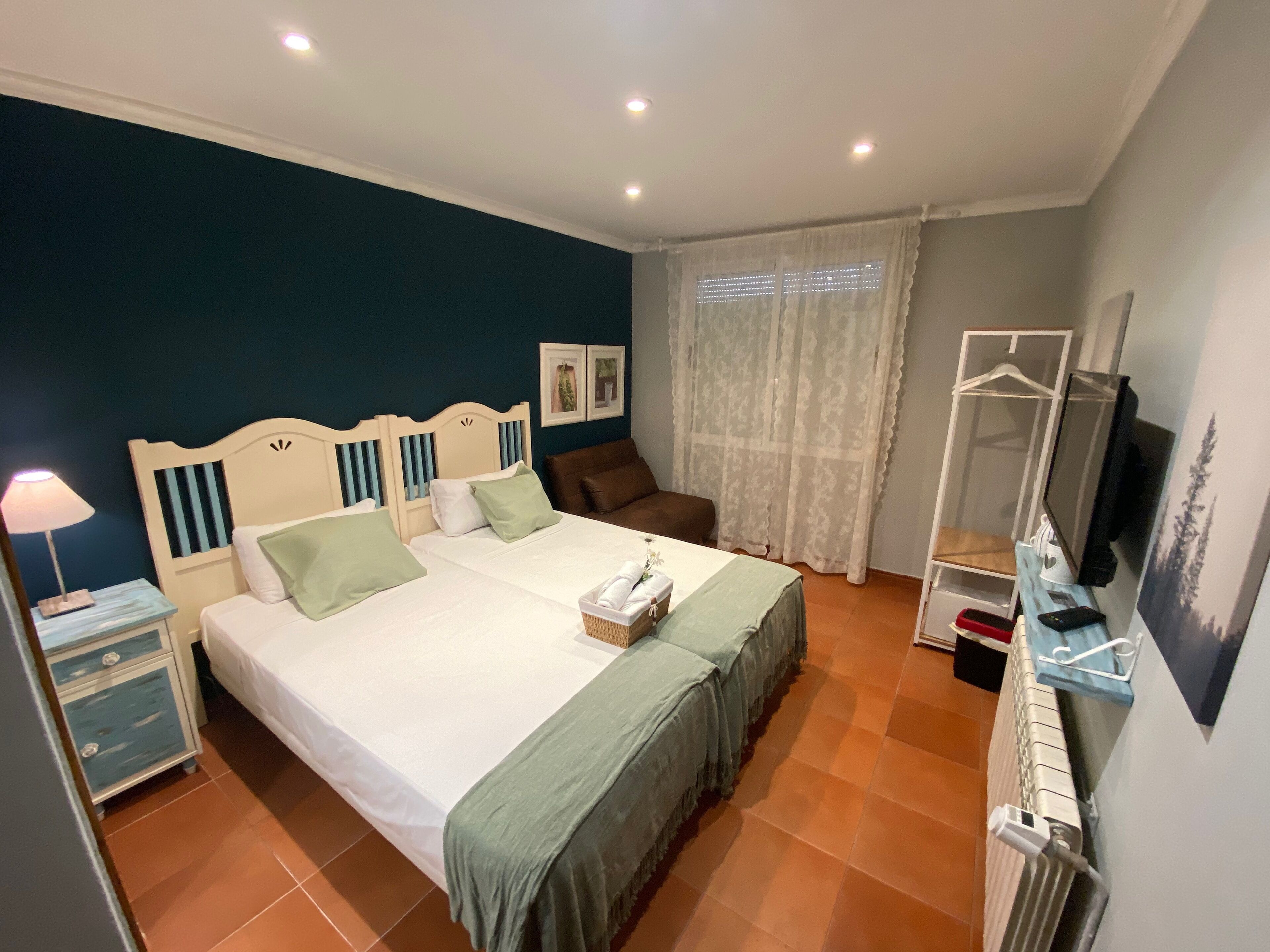 A bedroom with two beds, a nightstand, a dresser, a television, and a window with curtains.