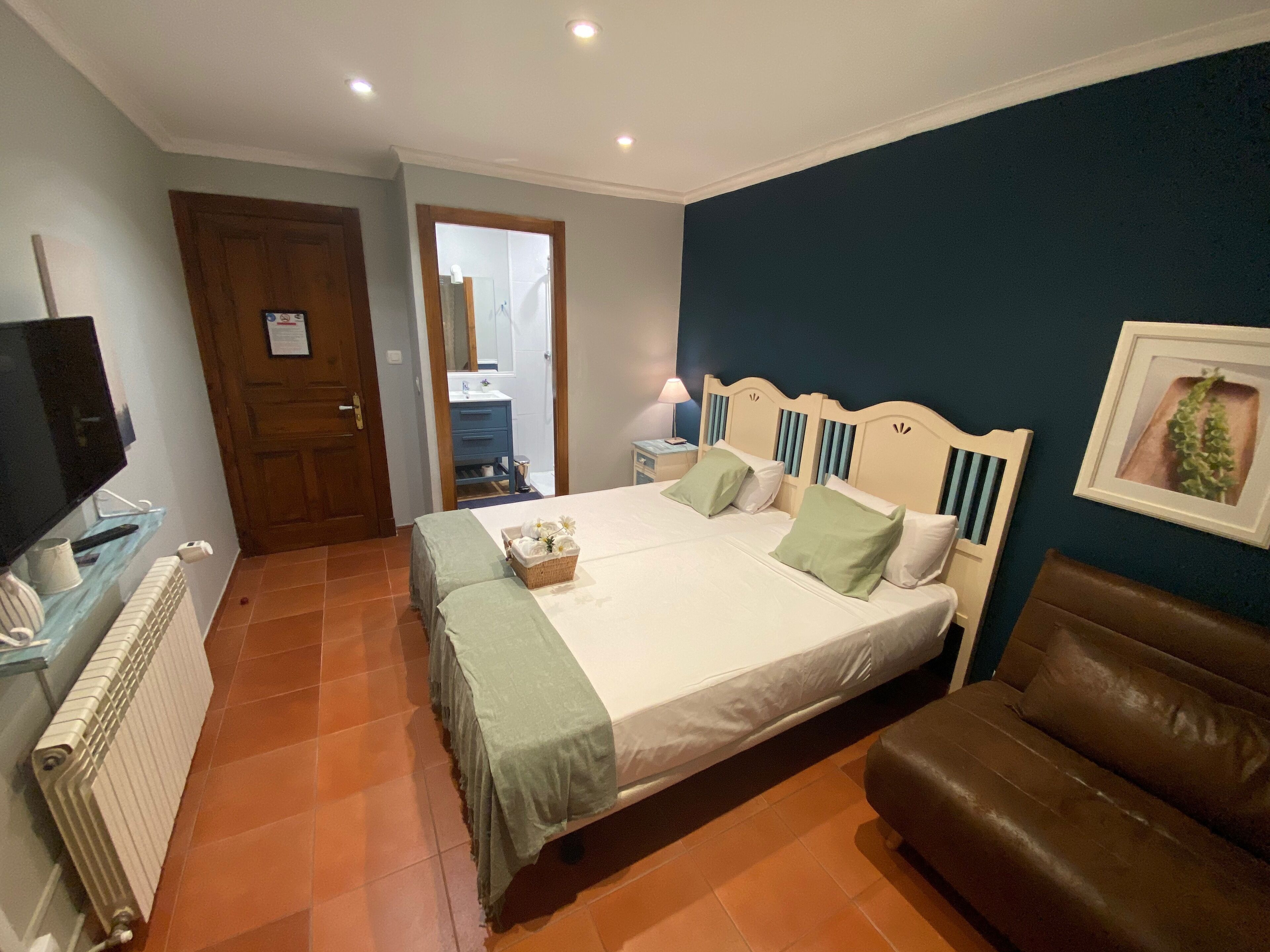 A bedroom with a bed, a television, a dresser, a brown leather chair, and a blue wall.