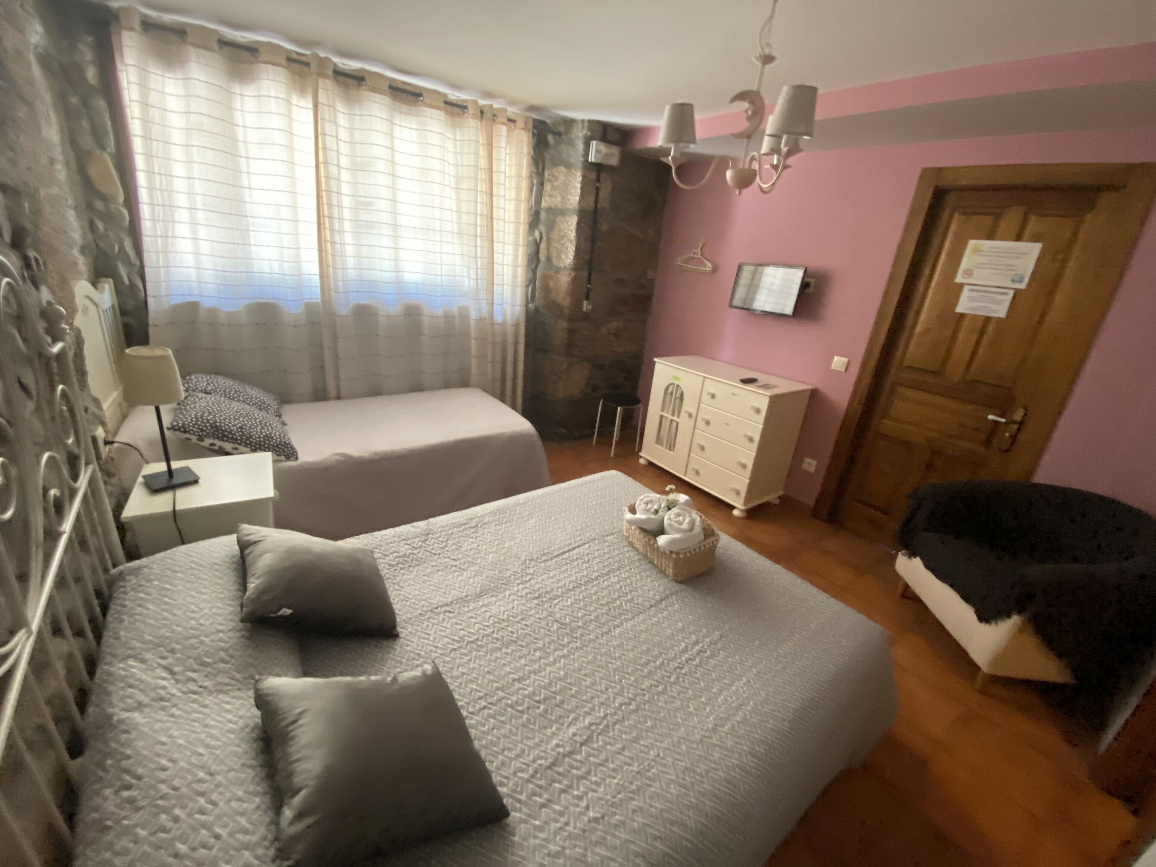 A bedroom with two beds, a dresser, a chair, a desk, and a television on the wall.