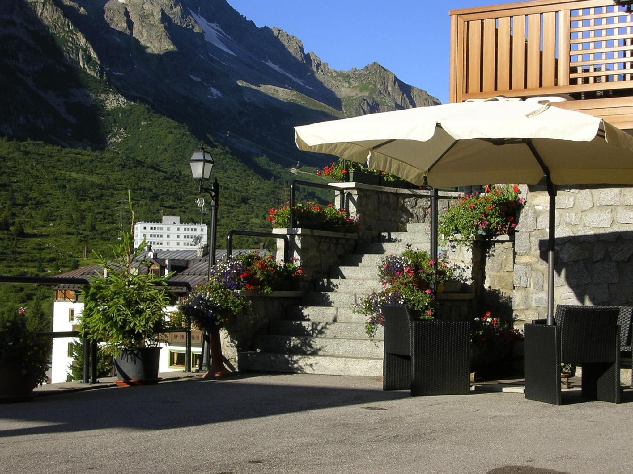 An outdoor seating area with a stone staircase, potted plants, and a wooden deck overlooking a mountainous landscape.