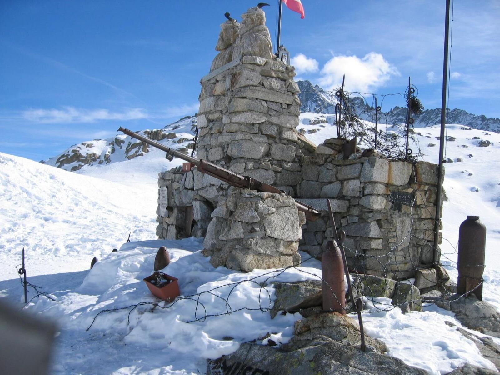 A stone structure with a flag, surrounded by snow and mountains.
