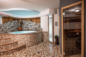 A spa area with a stone-tiled floor, a hot tub, and a wooden staircase. - Hotel Orchidea (Vermiglio)
