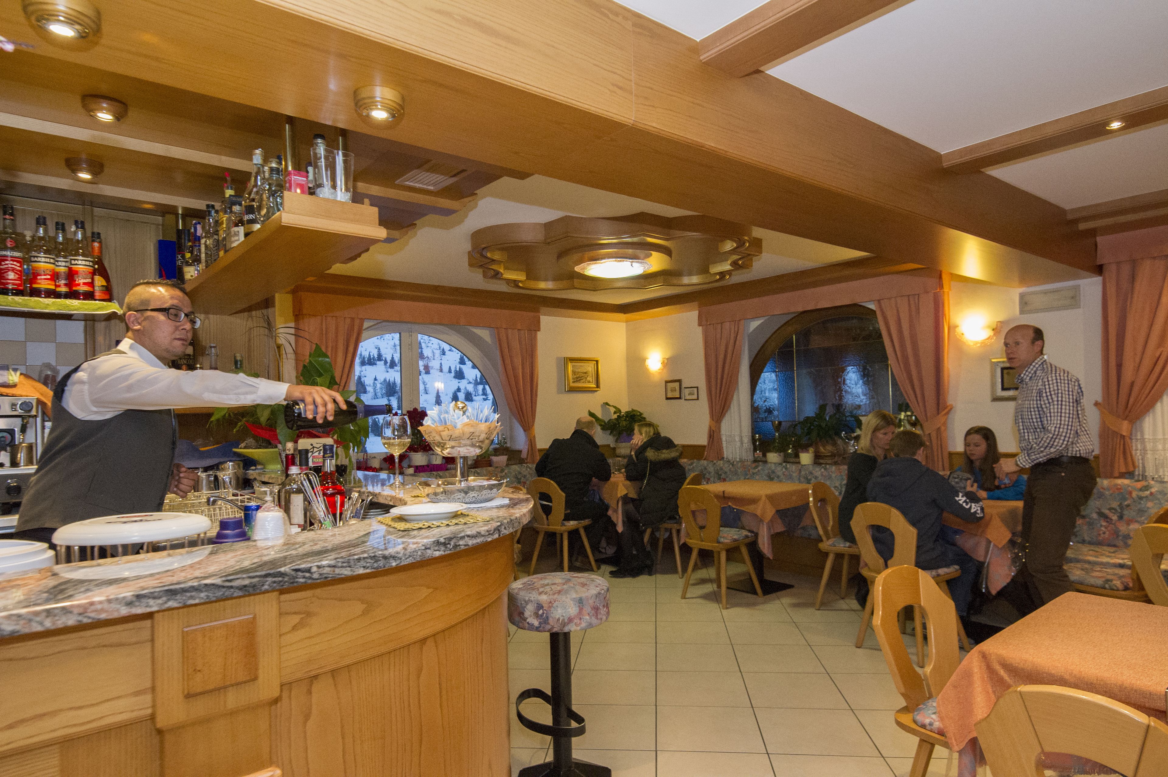 A bar area with a bartender, a counter with various bottles, and a seating area with tables and chairs.