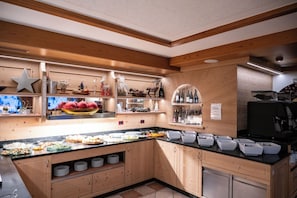 A kitchen with wooden cabinets, a black countertop, and various food items displayed. - Hotel Orchidea (Vermiglio)