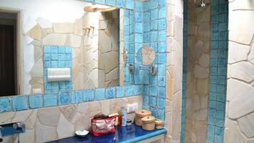 A bathroom with a stone and blue mosaic tile design, a sink with toiletries, and a shower area.