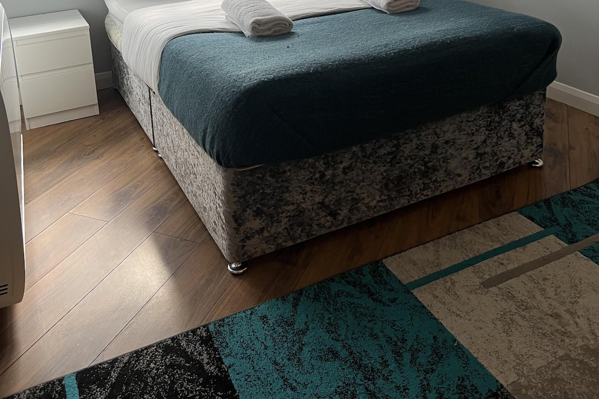 A bedroom with a bed, a nightstand, a window, and a painting on the wall.