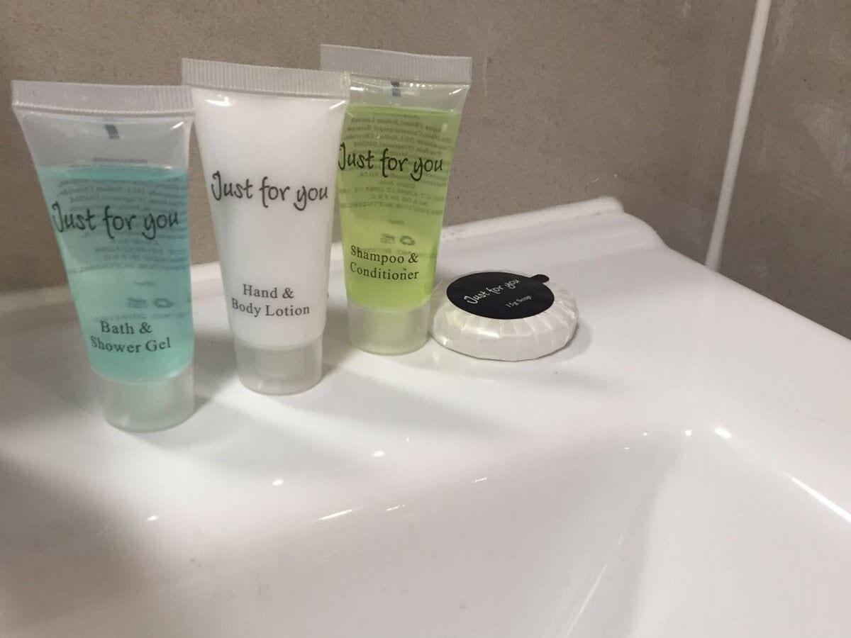 Trois produits de toilette sont posés sur le lavabo de la salle de bain : un gel douche, une lotion pour les mains et le corps, et un shampooing avec après-shampooing.