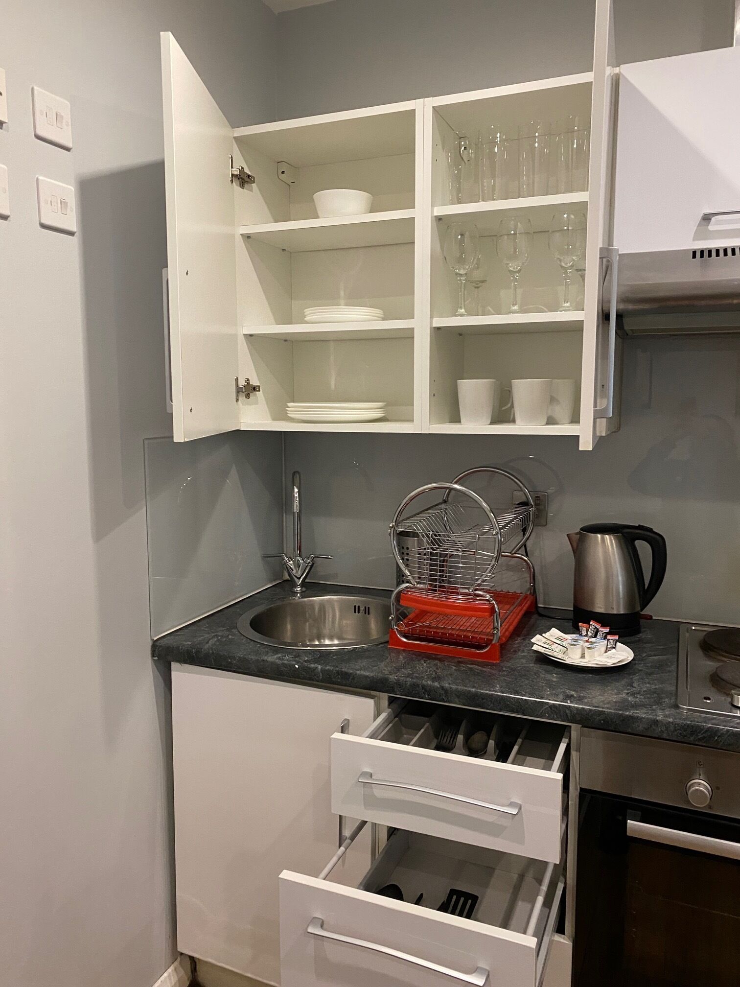 A kitchen with a stainless steel sink, a kettle, and a dish rack.