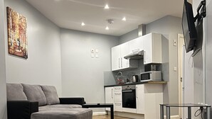 A modern living room with a grey sofa, a coffee table, and a kitchen area with white cabinets and appliances. - Showcase Apartments Kimberley House (Leicester)