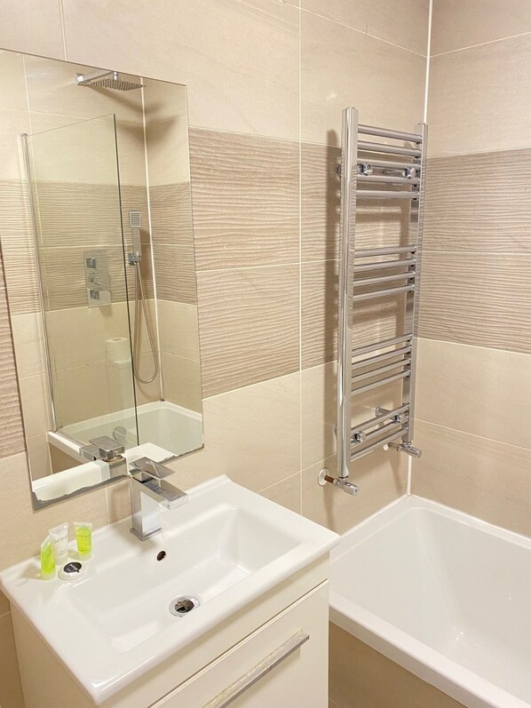 Un baño con ducha envuelta en vidrio, lavamanos blanco con espejo y toallero cromado.