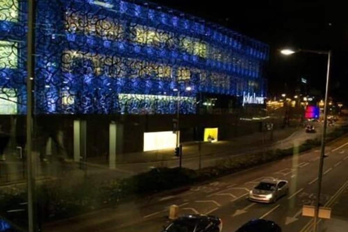 A building with a distinctive blue patterned facade, a street with cars, and a clear night sky.