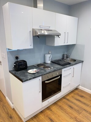 A compact kitchen with white cabinets, a stainless steel range hood, a built-in oven, a sink, and a toaster.