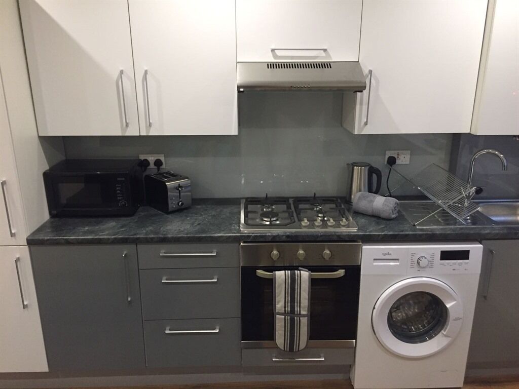 A compact kitchen with a microwave, toaster, gas stove, oven, and a washing machine.