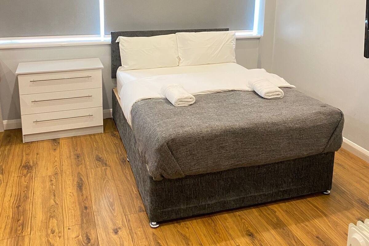 A modern bedroom with a bed, bedside tables, and a window with blinds.