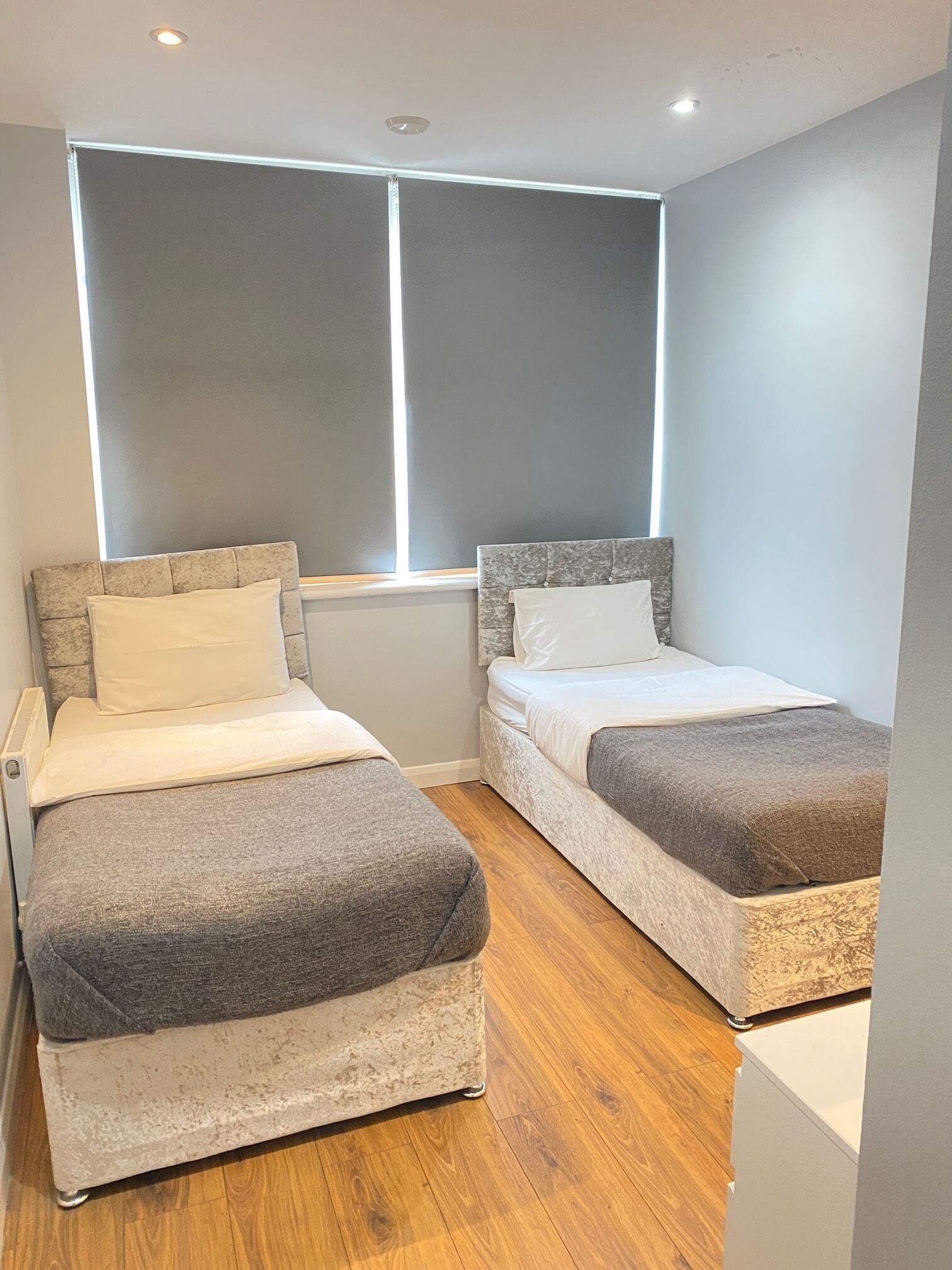A small, modern bedroom with two single beds, a window, and a wooden floor.