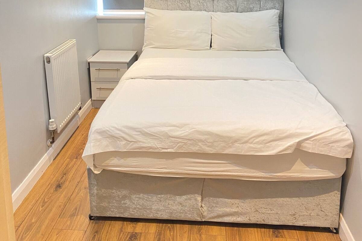 A bedroom with a bed, a nightstand, a radiator, and a window.