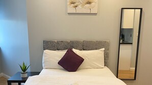 A neatly made bed with a teal bedspread, white pillows, and a maroon accent pillow. There are three rolled towels on the bed. A small potted plant is on a side table next to the bed. - Showcase Apartments Kimberley House (Leicester)