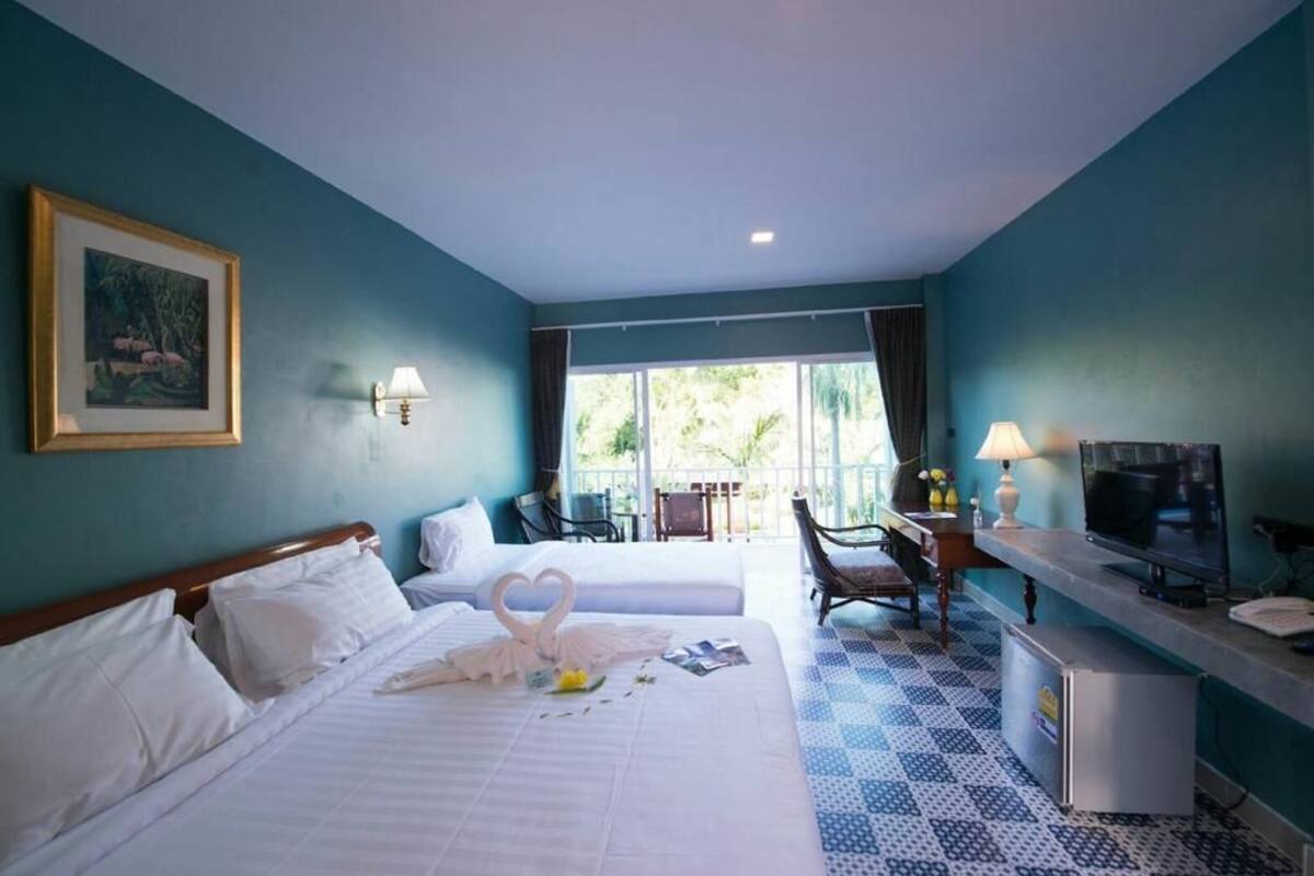 A hotel room with two beds, a desk with a TV, a chair, and a window with a view of greenery.