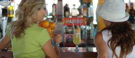 Dos personas sentadas en un bar con bebidas y naranjas.