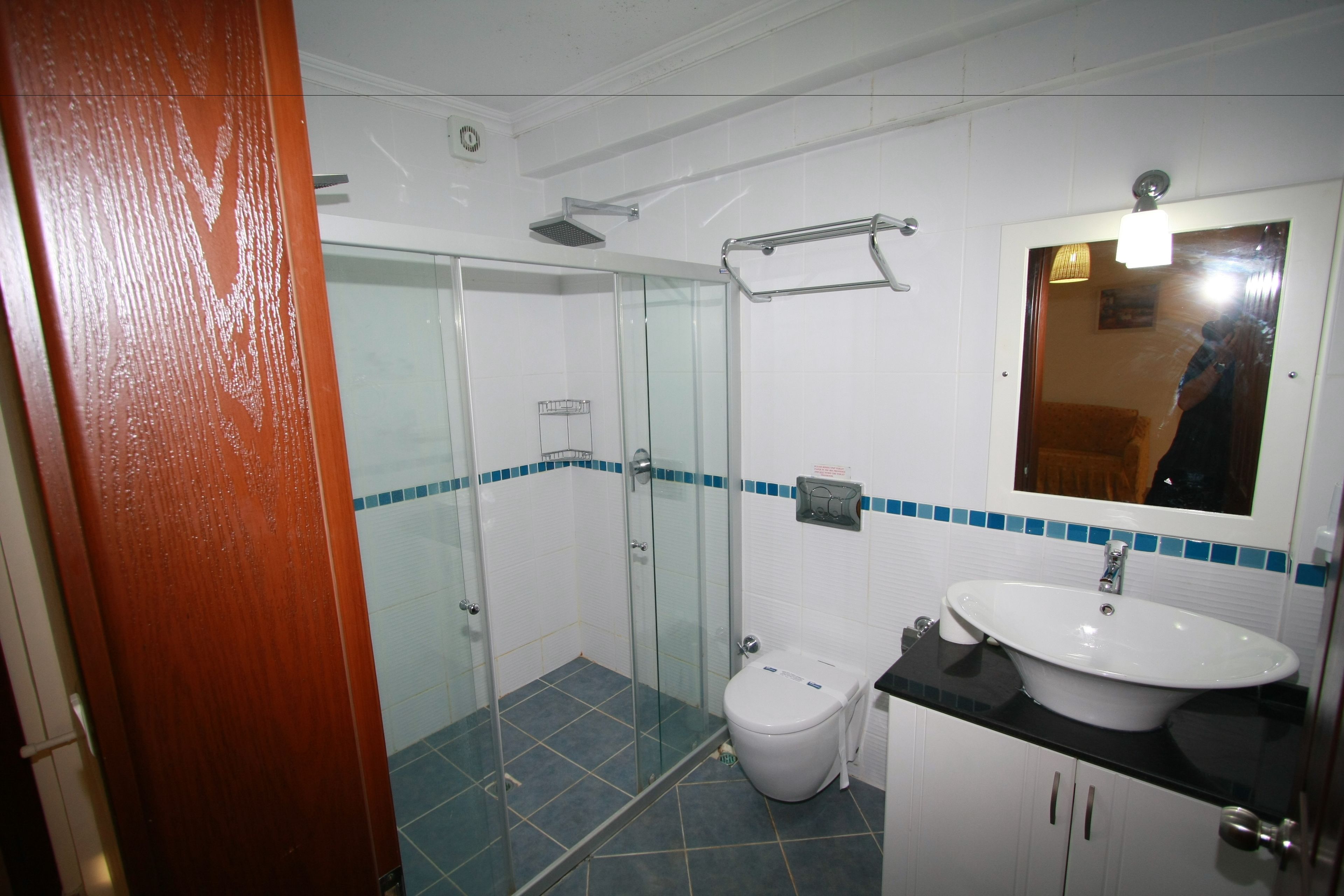 A bathroom with a glass-enclosed shower, a white toilet, a sink with a mirror above it, and a tiled floor.