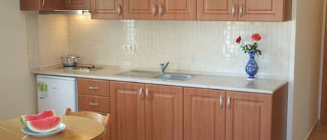 A kitchen with wooden cabinets, a white countertop, a sink, a dishwasher, and a table with a plate of watermelon.