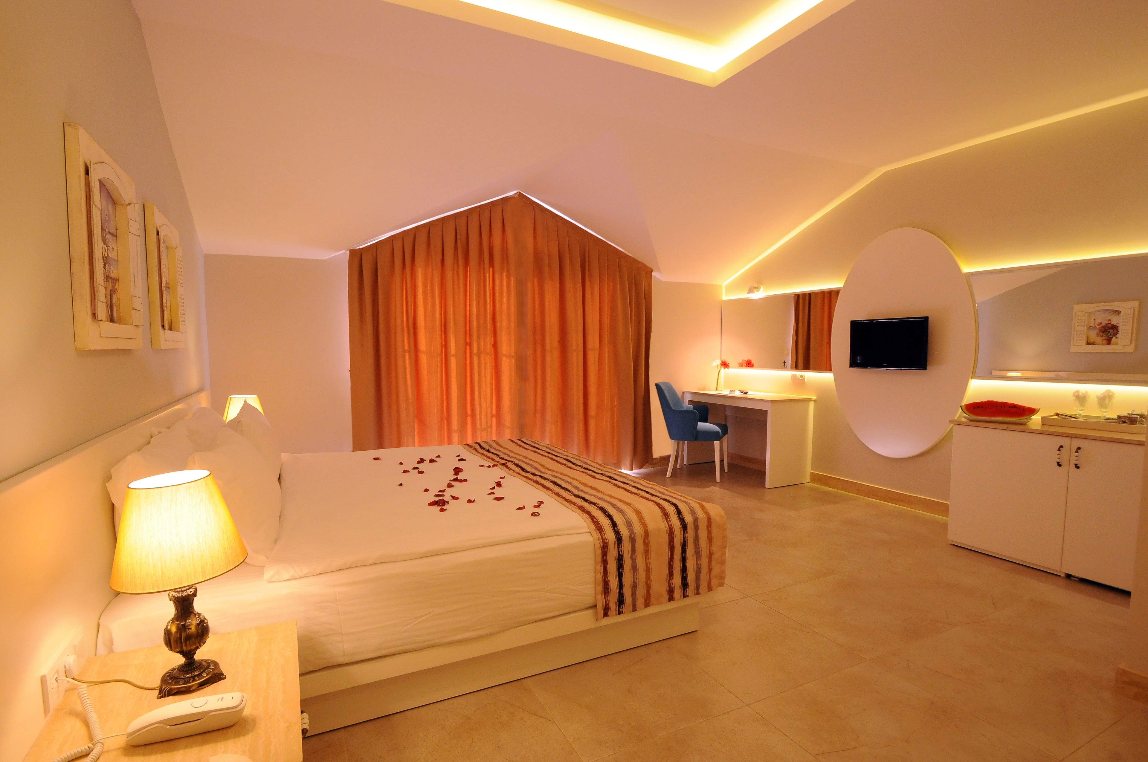 A hotel room with a bed, bedside table with a lamp, a desk with a chair, a television, and a cabinet.
