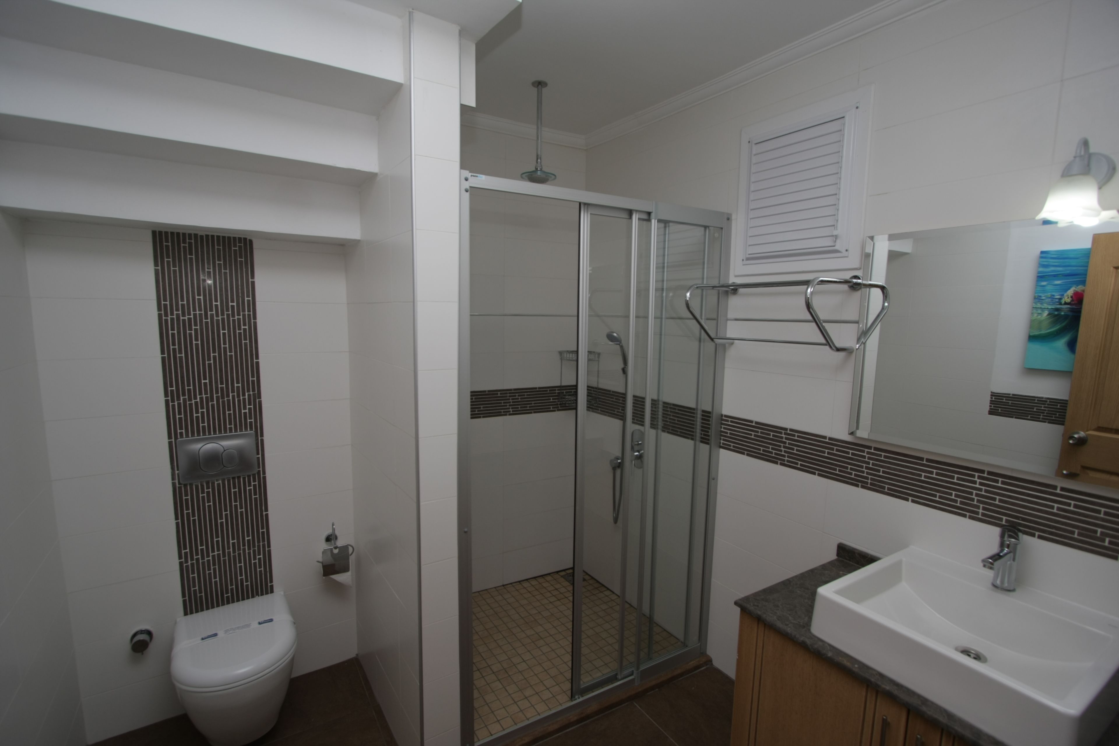 A bathroom with a toilet, a glass shower enclosure, a sink, and a mirror.