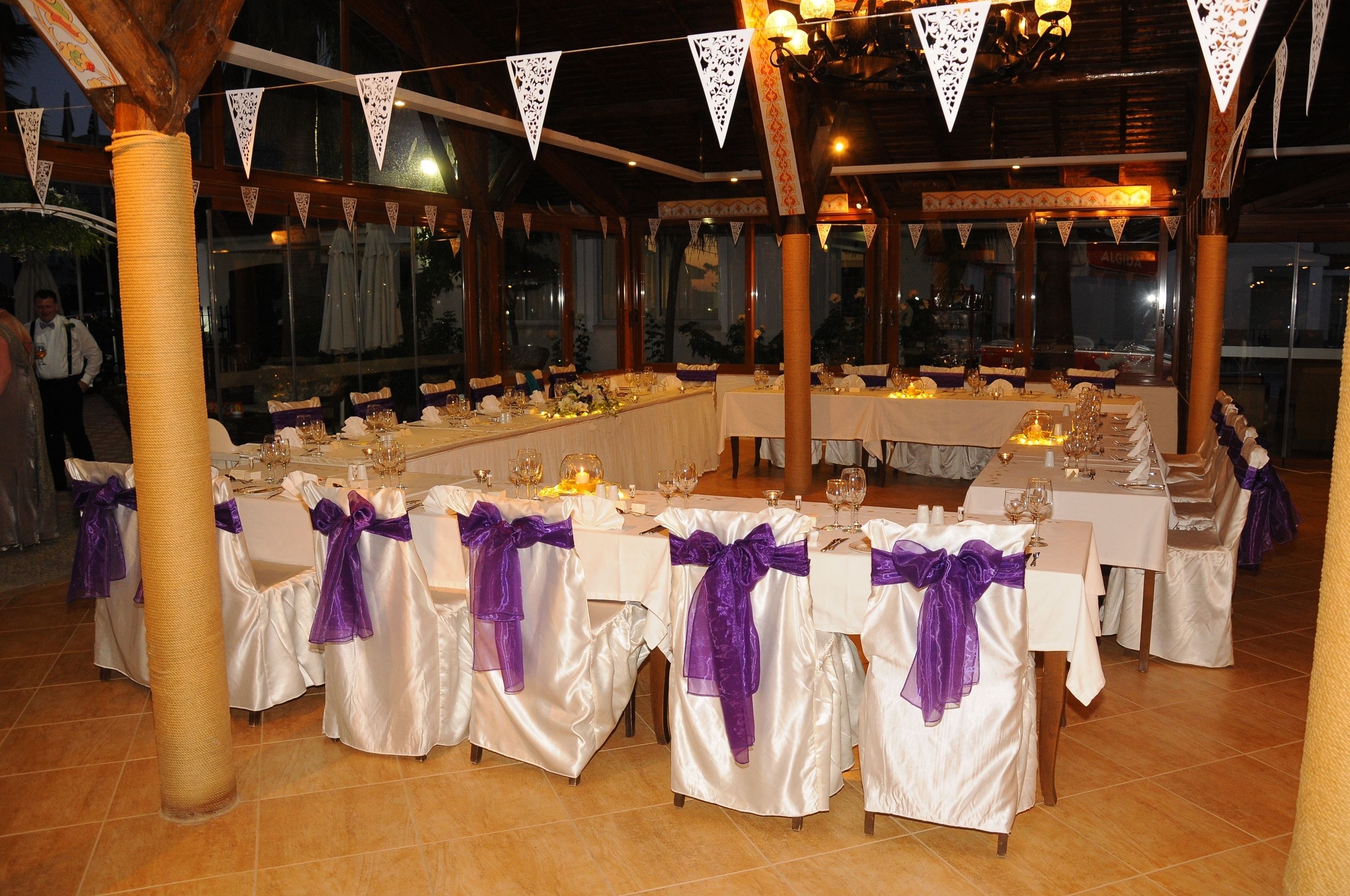 A banquet hall with long tables set for a formal event, decorated with white tablecloths and purple sashes.