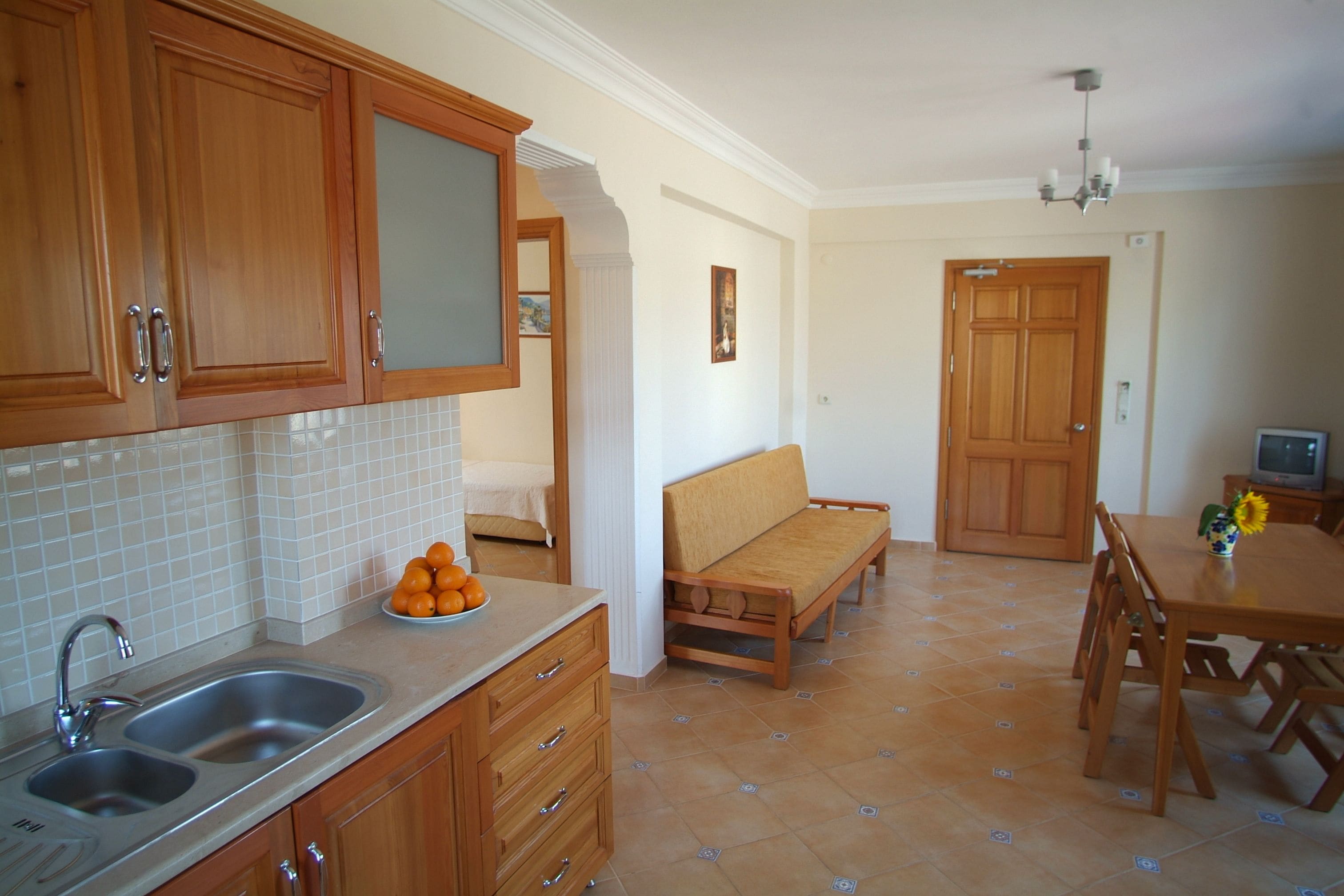 A kitchen with wooden cabinets, a double sink, and a dining area with a wooden table and chairs.