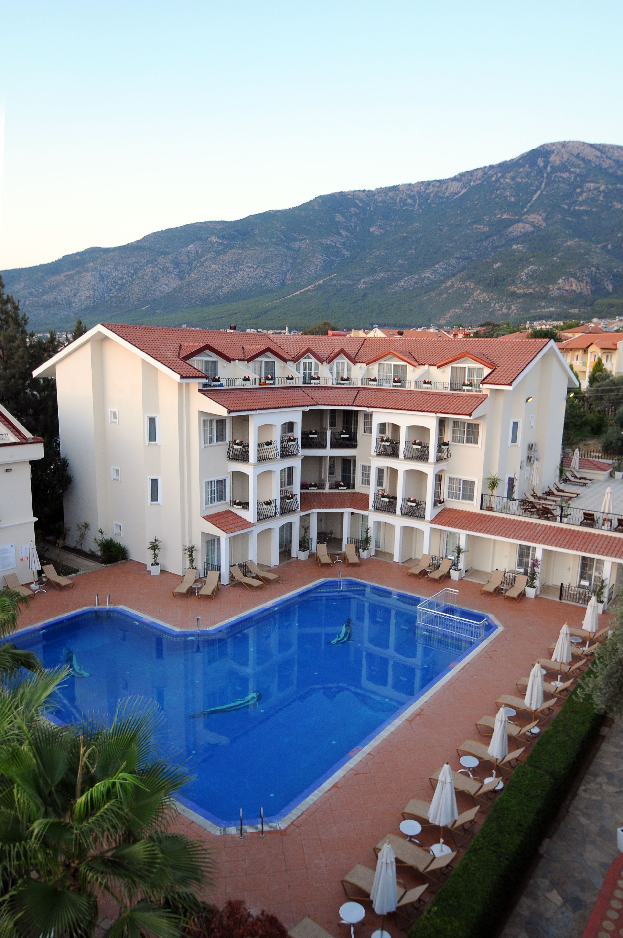 A hotel with a swimming pool, multiple balconies, and a mountainous backdrop.