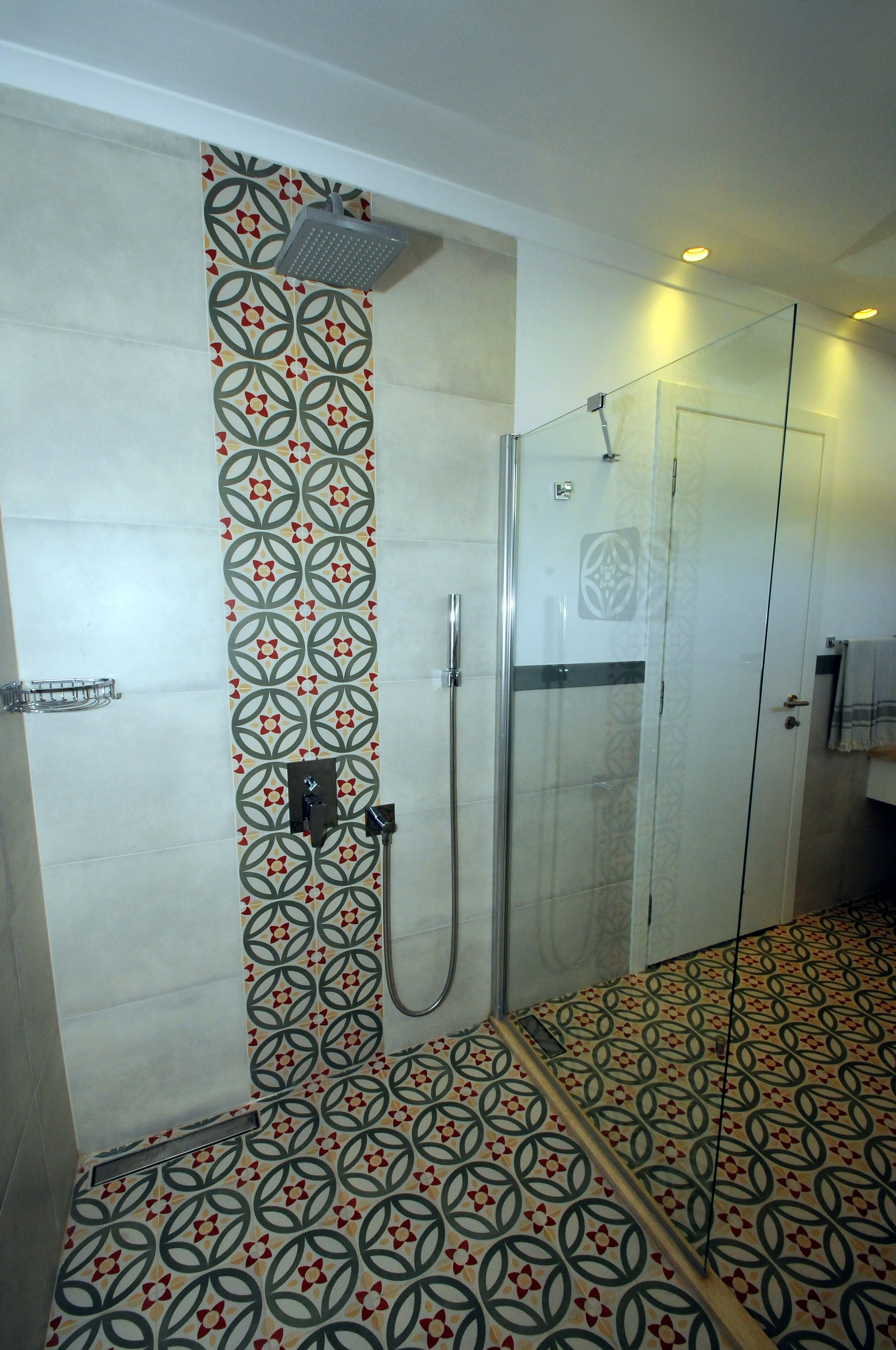 Eine Dusche mit Glastür, ein gemusterter Boden und eine Wand mit geometrischem Muster.