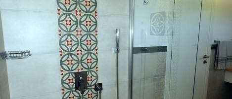 A shower with a glass door, a patterned floor, and a wall with a geometric design.