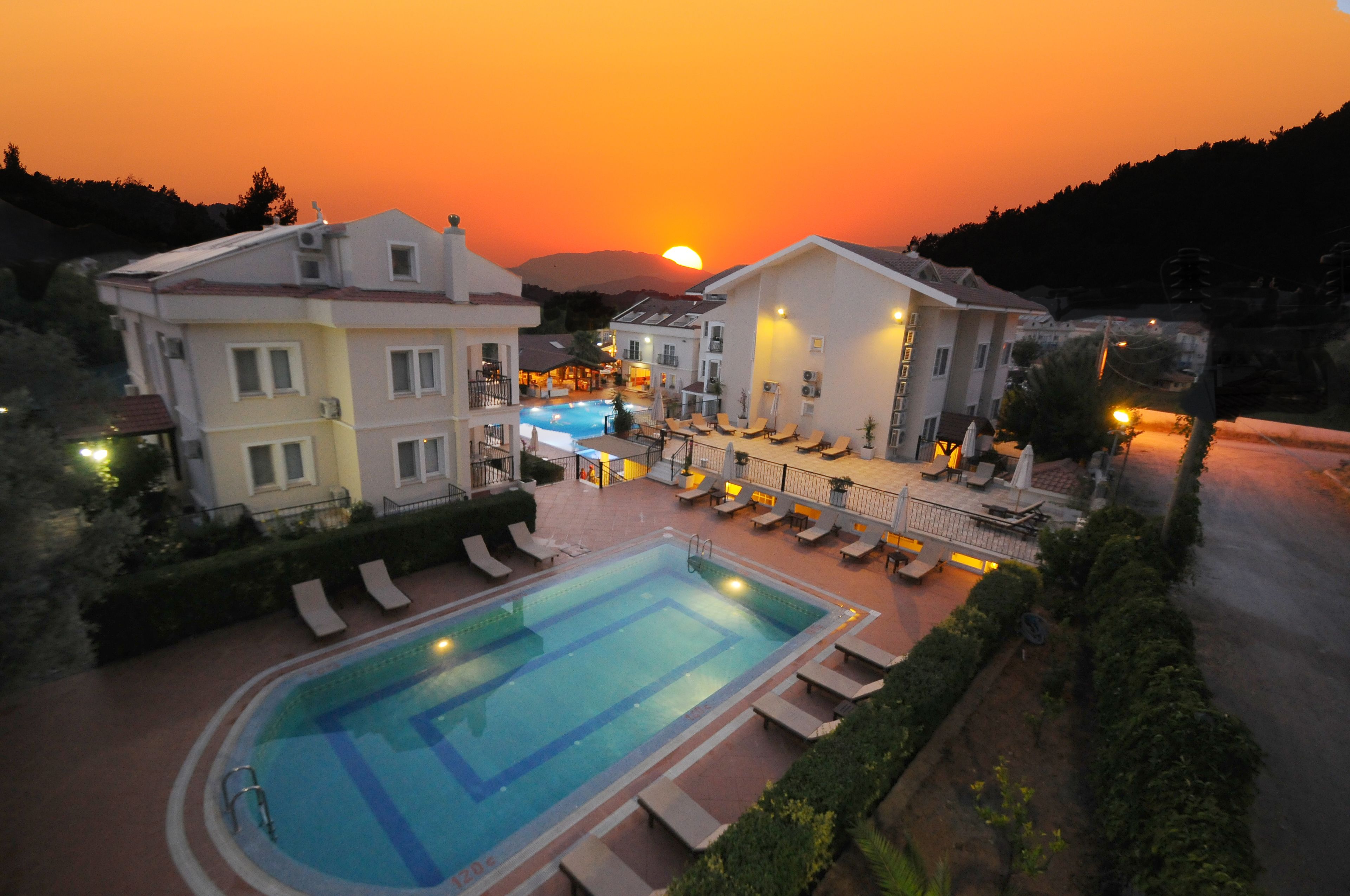 A hotel with a swimming pool, lounge chairs, and a sunset view.