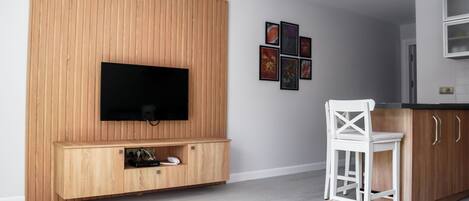 A modern living room with a wooden TV stand, a flat-screen TV, a white chair, and a glass coffee table.