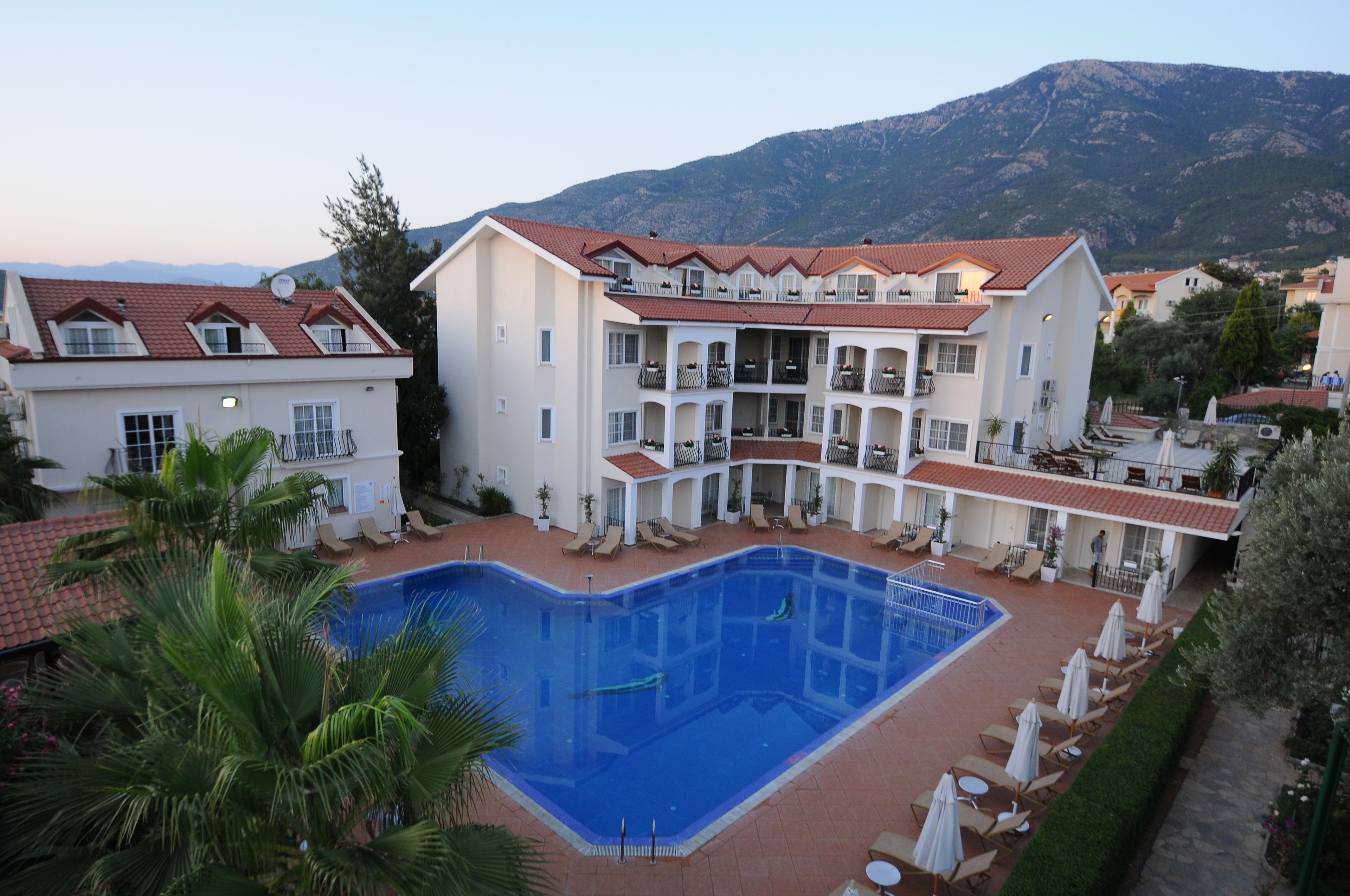 A hotel with a swimming pool, multiple balconies, and a mountainous backdrop.