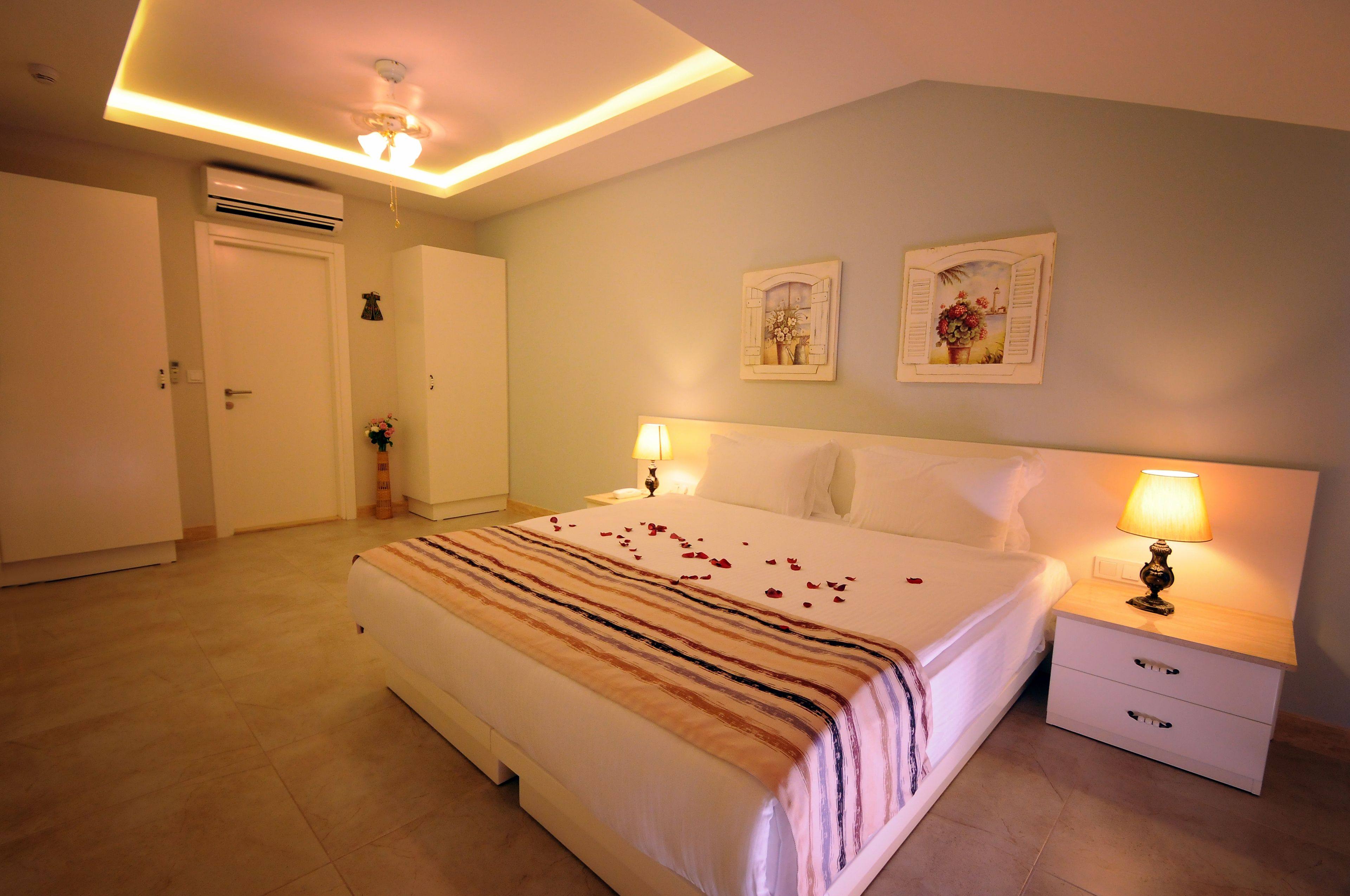 A hotel room with a large bed, bedside tables with lamps, a ceiling fan, and an air conditioning unit.