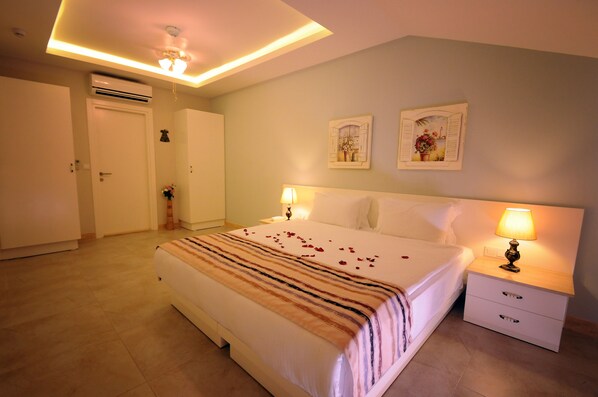 A hotel room with a large bed, bedside tables with lamps, a ceiling fan, and an air conditioning unit.