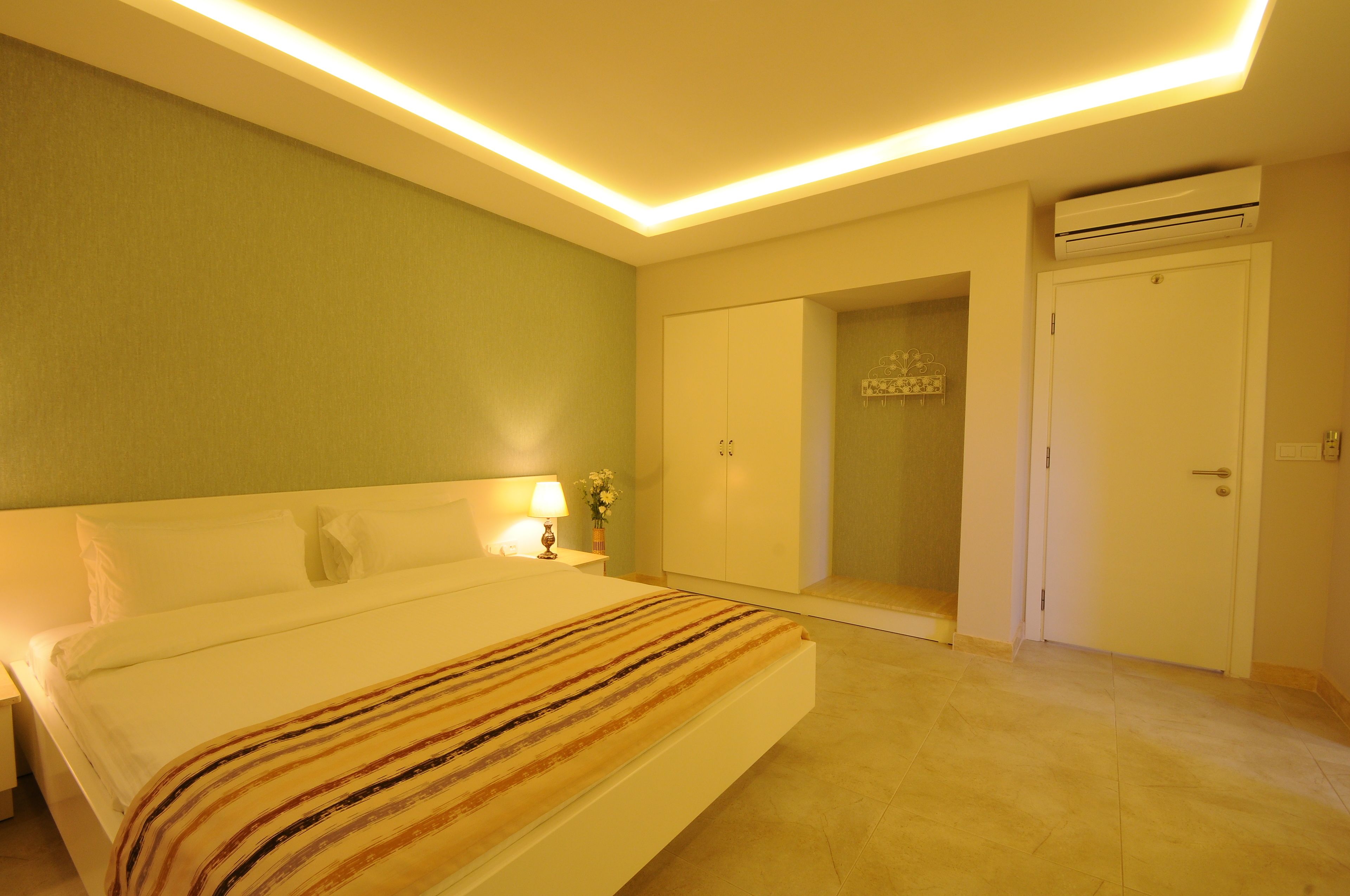 A hotel room with a bed, a nightstand with a lamp, a wardrobe, and an air conditioning unit.