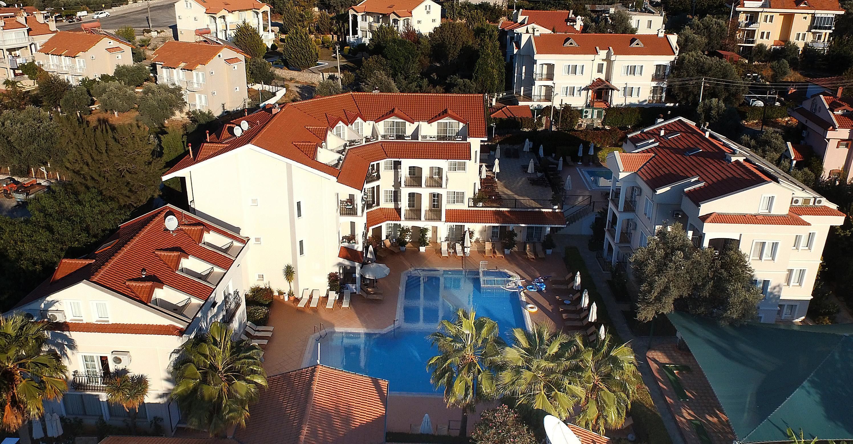 Vista aérea de una zona residencial con piscina rodeada de casas con tejados de tejas rojas.
