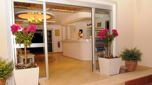 Eine Hotelhalle mit Empfangstresen, einer Kristallleuchter und Pflanzen in Töpfen.