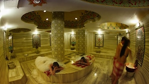Ein traditionelles Badezimmer mit mehreren Badewannen und einer zentralen Säule, umgeben von Wänden und Decken mit Musterverzierungen.