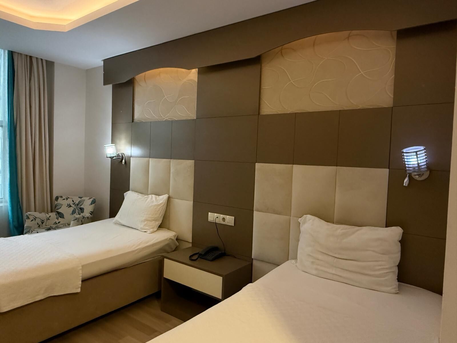 Habitación de hotel con dos camas, una mesita de noche con teléfono y una lámpara fijada a la pared.