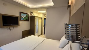 Ein Hotelzimmer mit Bett, Wandfernseher, Tür zu einem Badezimmer und Duschbereich.