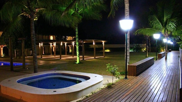 A nighttime outdoor area with a hot tub, wooden deck, palm trees, and illuminated structures. - Pousada Porto do Rio (Caraguatatuba)