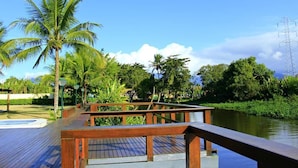 A wooden deck with a view of a calm river and palm trees. - Pousada Porto do Rio (Caraguatatuba)