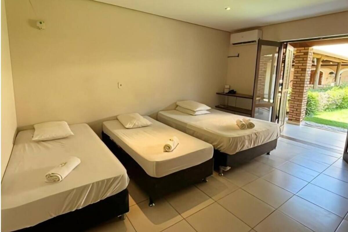 Ein Hotelzimmer mit drei Einzelbetten, Fliesenboden und Blick ins Freie.