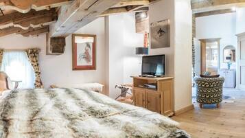 A cozy room with a large fur-covered bed, wooden beams, a television on a wooden stand, and a patterned ottoman.